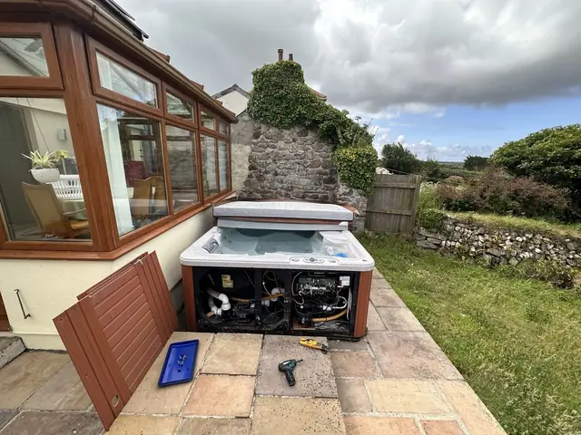 Hot tub with its side panels off for repair on a garden patio, with tools and a parts tray beside it