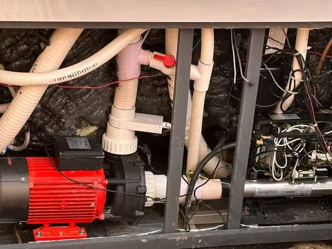 Inside a hot tub equipment bay: the red pump, heater, control pack and pipework