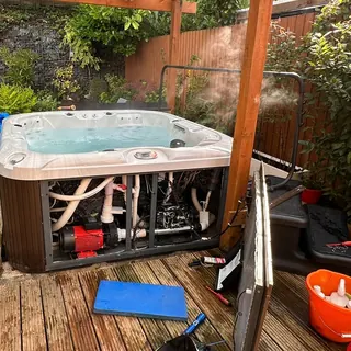 Hot tub under a timber pergola with its side panels off and the pump and plumbing exposed during a repair